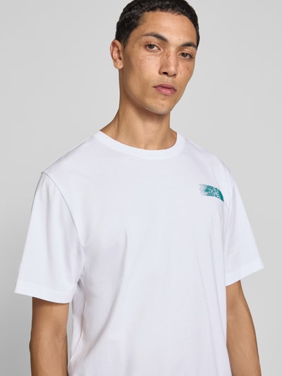 Męski model nosi Relaxed Fit T-Shirt mit Logo-Print von The North Face z bawełny, okrągły dekolt, Ganzkörperansicht z przodu, długość tyłu 71 cm w rozmiarze M.