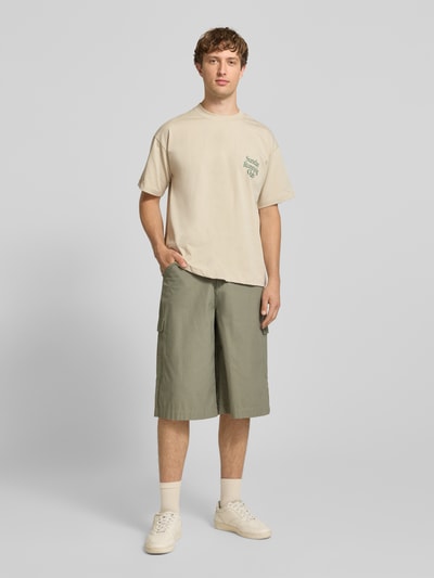 Męski model nosi T-Shirt mit Print und Rundhalsausschnitt od ANOTHER COTTON LAB z bawełny, krój relaxed fit, długość tyłu 69 cm, widok całej sylwetki z przodu.