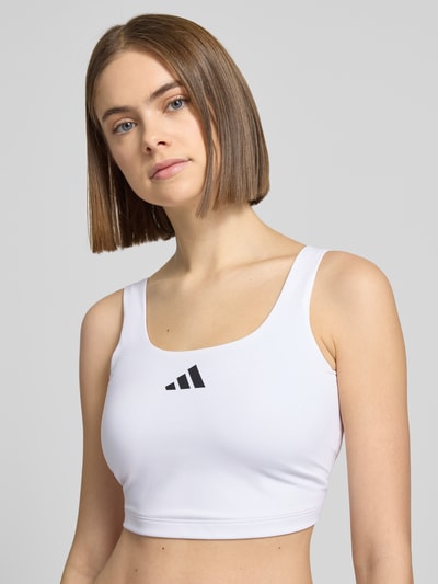 Vrouwenmodel draagt 'BH met Label-Print' van adidas Sportswear in wit, nauwsluitende pasvorm, stretchmateriaal, label-print, close-up bovenlichaam