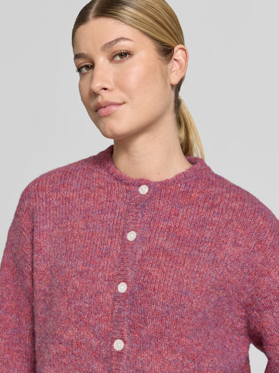 Frauenmodel trägt Relaxed Fit Strickjacke mit Woll-Anteil Modell 'Belablue' von ICHI, rosa-lila meliert, Knopfleiste, Struktur, Nahaufnahme Oberkörper.