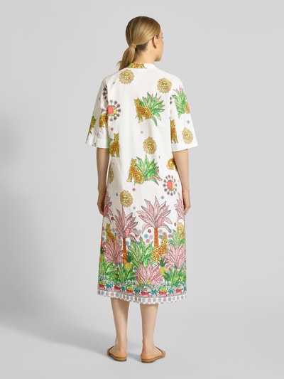Frauenmodel trägt Midikleid mit V-Ausschnitt von Emily Van den Bergh aus reiner Baumwolle, weiß mit buntem Blumen- und Leopardendruck, gerader Schnitt, 3/4-Arm, Seitenschlitz, Ganzkörperansicht Rückansicht.