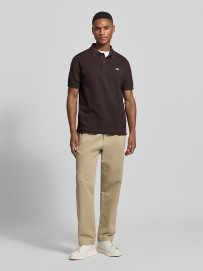 Männermodel trägt Regular Fit Poloshirt aus reiner Baumwolle von Lacoste, unifarben, Logo-Stitching, Piqué-Textur, Ganzkörperansicht von vorne.