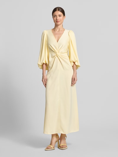 Frauenmodel trägt Maxikleid mit Ballonärmeln Modell 'THEA' von YAS, gelb, Material-Mix mit Stretch-Anteil, Taillierter Schnitt, V-Ausschnitt, Knoten-Detail, Ganzkörperansicht von vorne.