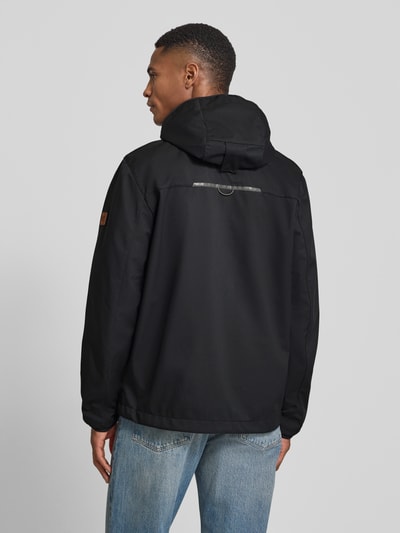 Männermodel trägt Jacke mit Reißverschlusstaschen von camel active in Schwarz, Kapuze, elastische Ärmel, Rückenlänge 71 cm, Ganzkörperansicht Rückansicht.