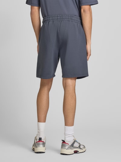 Männermodel trägt Shorts mit elastischem Bund und Logo-Stitching von Pegador aus Baumwoll-Mix in Loose-Fit, Ganzkörperansicht Rückansicht.