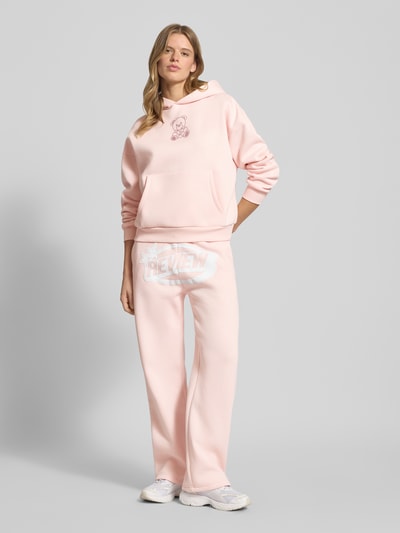 Frauenmodel trägt Straight Leg Sweatpants mit Logo und elastischem Bund von Review, hellrosa, Baumwoll-Mix, Ganzkörperansicht von vorne.