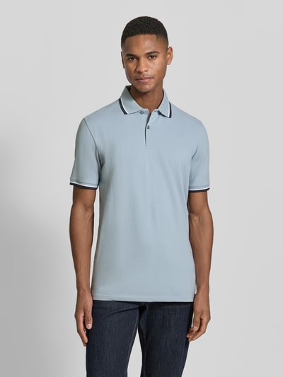 Männermodel trägt Slim Fit Poloshirt aus Bio-Baumwoll-Mix Modell 'SLIM ATLAS SPORT' von SELECTED HOMME in Hellblau, Ganzkörperansicht von vorne. Einfarbiges Design mit Kontraststreifen, kurzer Knopfleiste und Rippen am Ärmel, schlanke Passform, Piqué-Struktur.