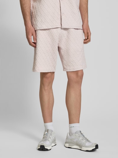Męski model nosi Relaxed Fit Sweatshorts mit Strukturmuster model 'Jovren' od Pegador, elastyczna mieszanka materiałów z mieszanką bawełny, jasnoróżowy kolor, fakturowany wzór, szerokość w rozmiarze M: 39 cm, długość wewnętrzna nogawki w rozmiarze M: 24 cm, ujęcie: Ganzkörperansicht z przodu.