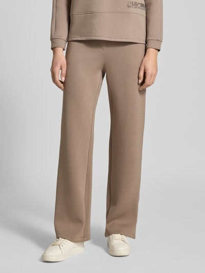 Frauenmodel trägt Stoffhose mit elastischem Bund von Betty Barclay, Viskose-Mix mit Stretch-Anteil, lockerer Schnitt, Label-Detail, französische Eingrifftaschen, Gesäßtaschen, beige einfarbig, weiche Struktur, Ganzkörperansicht von vorne.