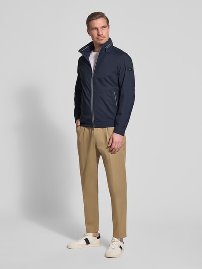 Männermodel trägt Regular Fit Jacke mit Stehkragen von bugatti in donkerblauw met logodetail, steekzakken, tweewegritssluiting, elastische mouwboord, verstopte capuchon, regular fit, ruglengte 68 cm, schouderbreedte 42 cm, borstwijdte 50 cm, mouwlengte 65 cm, ganzkörperansicht von vorne
