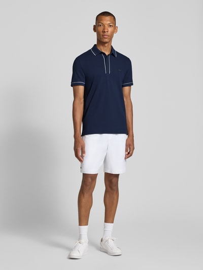 Mannenmodel draagt donkerblauw Regular Fit poloshirt uit katoenmix van Lacoste, witte shorts, sneakers, volledige vooraanzicht