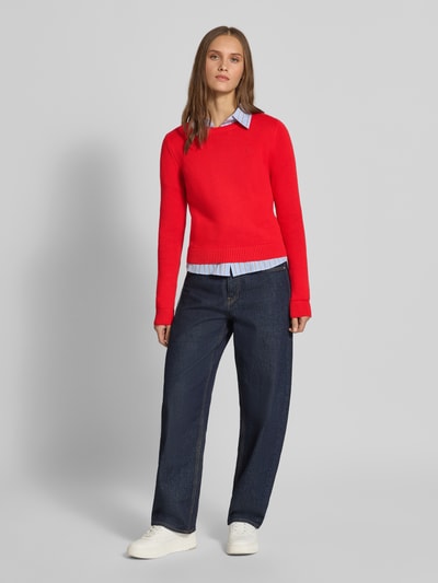 Frauenmodel trägt Slim Fit Pullover aus reiner Baumwolle von REVIEW in Rot, Strick-Optik, kombiniert mit Jeans, Ganzkörperansicht von vorne. Rückenlänge bei Größe S: 54 cm, Ärmellänge bei Größe S: 72 cm, Logo-Stitching sichtbar.