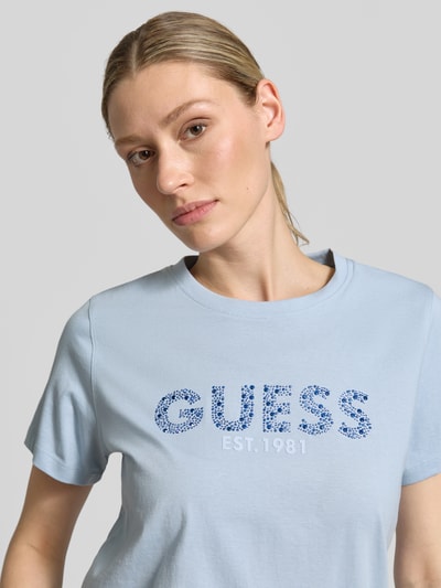 Vrouwenmodel draagt T-shirt met Label-Print en Strasssteinbesatz van guess in lichtblauw, puur katoen, straight fit, ronde hals, labelprint met strass-steentjes, ruglengte maat S 59 cm, Nahaufnahme bovenlichaam.
