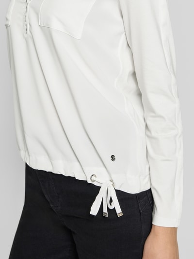 Frauenmodel trägt Regular Fit Bluse mit Brusttaschen von monari, weiß, Ziersteinbesatz, Tunika-Ausschnitt, langärmelig, Nahaufnahme Oberkörper.