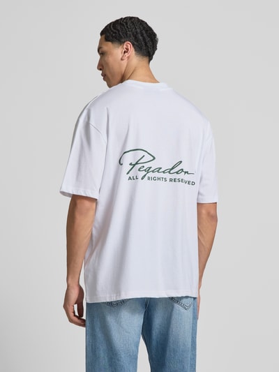Männermodel trägt Oversized T-Shirt aus reiner Baumwolle Modell 'Pike' von Pegador, Label-Stitching, Rückenlänge 71 cm, Ganzkörperansicht Rückansicht.