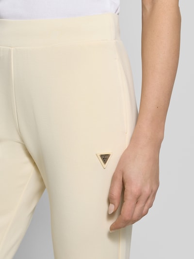 Frauenmodel trägt Sweatpants mit Label-Detail Modell 'OLYMPE' von Guess Activewear in Creme, glatte Oberfläche, körpernaher Schnitt, Nahaufnahme Oberschenkel.