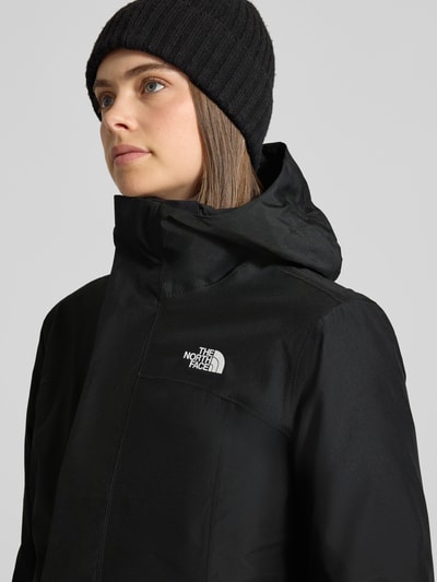 Vrouwenmodel draagt zwarte lange jas met capuchon Model 'SUZANNE' van The North Face, labeldetail en ritssluiting, Nahaufnahme Oberkörper