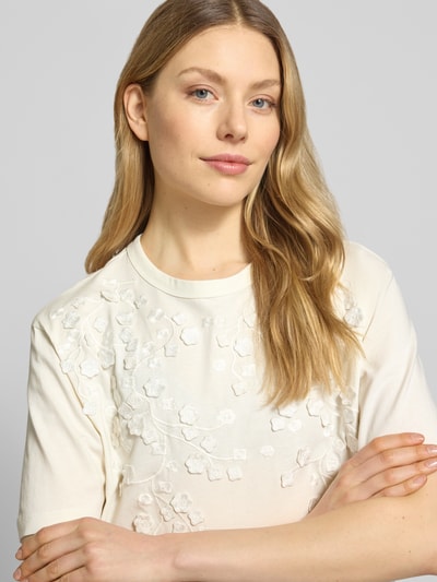 Frauenmodel trägt T-Shirt mit Rundhalsausschnitt von JAKE*S STUDIO WOMAN in Creme mit Blumenstruktur, reine Baumwolle, Nahaufnahme Oberkörper.