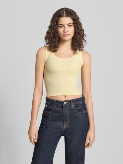 Frauenmodel trägt Slim Fit Top mit Logo-Detail von ANOTHER COTTON LAB, gelb, elastischer Baumwoll-Mix, Rundhalsausschnitt, Nahaufnahme Oberkörper.