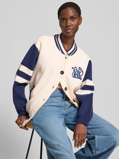 Frauenmodel trägt Relaxed Fit Jacke mit Viskose-Anteil von BAUM & PFERDGARTEN in Creme und Dunkelblau, Logo-Stitching, Eingrifftaschen, durchgängige Knopfleiste, Baumwoll-Mix mit Viskose- und Kaschmir-Anteil, Ganzkörperansicht von vorne.