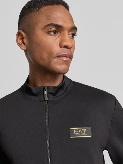 Męski model nosi Bluza rozpinana z zamkiem błyskawicznym dwustronnym od EA7 Emporio Armani, mieszanka materiałów z dodatkiem wiskozy, krój regular fit, stójka, naszywka z logo, kieszenie zapinane na zamek błyskawiczny, długość tyłu 65 cm, długość rękawa 65 cm, widok na górną część ciała z przodu.