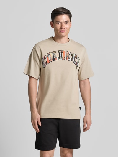 Männermodel trägt T-shirt met COLUCCI-logo van puur katoen, recht model, ronde hals, 1/2-mouwen, ruglengte maat M 72 cm, Ganzkörperansicht von vorne.