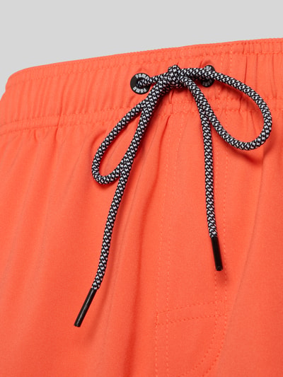 Produktfoto, Badeshorts mit Seitentaschen und Reißverschlusstasche hinten von PUMA in Orange, strukturierte Oberfläche, elastischer Bund, Nahaufnahme Oberkörper.