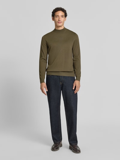 Männermodel trägt Regular Fit Pullover aus reiner Schurwolle Modell 'Davide' von JOOP! COLLECTION in Oliv, glatte Textur, Ganzkörperansicht von vorne.