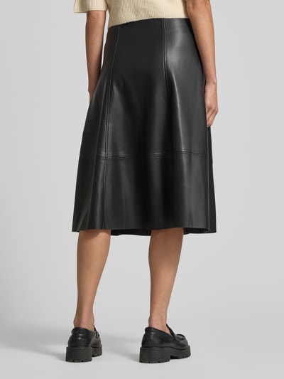 Frauenmodel trägt Midirock in Leder-Optik Modell 'BECKIE' von Soyaconcept, schwarze A-Linie mit Teilungsnähten, Ganzkörperansicht Rückansicht. Bundweite 40 cm, Gesamtlänge 70 cm bei Größe 36.