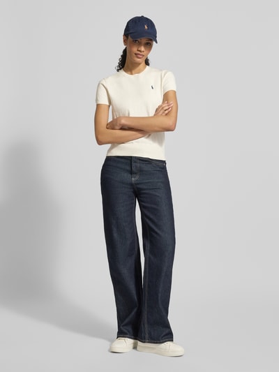 Frauenmodel trägt Regular Fit Kurzarmpullover aus Baumwoll-Mix von Polo Ralph Lauren in Creme, kombiniert mit dunkelblauer Hose, Ganzkörperansicht von vorne.