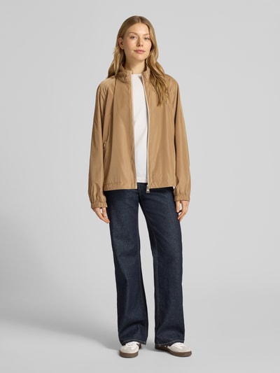 Frauenmodel trägt Jacke mit elastischen Abschlüssen und Stehkragen von Fuchs Schmitt in Beige, Gerader-Schnitt, Reißverschluss, Raglanärmel, Seitliche Reißverschlusstaschen, Rückenlänge 56 cm, Schulterbreite 38 cm, Brustweite 48 cm, Ärmellänge 43 cm, Ganzkörperansicht von vorne.