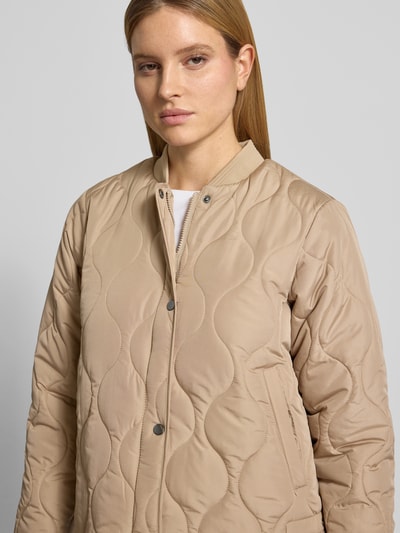Kobieta prezentuje kurtkę pikowaną o kroju regular fit ze stójką, model 'FENYA 78' od Soyaconcept, beżowe tony, listwa guzikowa, długość tyłu w rozmiarze S: 62 cm, szerokość ramion w rozmiarze S: 42 cm, szerokość klatki piersiowej w rozmiarze S: 53 cm, długość rękawów w rozmiarze S: 62 cm, faktura pikowania, całkowity widok przód