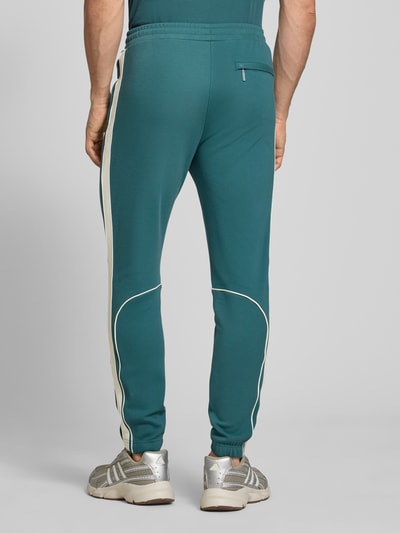 Männermodel trägt Slim Fit Tracksuit mit Logo-Stitching Modell 'Egeo' von SERGIO TACCHINI in Petrol mit weißen Akzenten, Rückansicht Ganzkörperansicht. Elastischer Baumwoll-Mix, Stehkragen, Reißverschluss, elastische Abschlüsse, Maßangaben für Größe M.