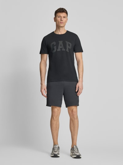 Männermodel trägt Sweatshorts mit elastischem Bund von GAP aus Baumwoll-Mix mit Logo, Relaxed-Fit, dunkle Farbe, Ganzkörperansicht von vorne.