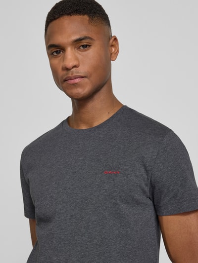 Männermodel trägt T-Shirt mit Label-Detail von Gant in Dunkelgrau, reine Baumwolle, gerader Schnitt, Nahaufnahme Oberkörper.