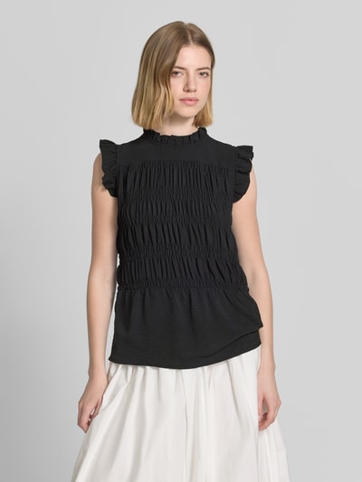 Frauenmodel trägt Blusentop mit Rüschenkragen Modell 'CATH' von Soyaconcept, schwarz, Körpernaher-Schnitt, Rüschenärmel, Smok-Detail, Ganzkörperansicht von vorne.