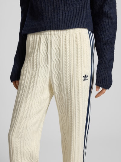 Vrouwenmodel draagt Loose Fit Strickhose uit viscosemix van adidas Originals met elastische band, logostitching en galonstrepen. Nahaufnahme Oberkörper.