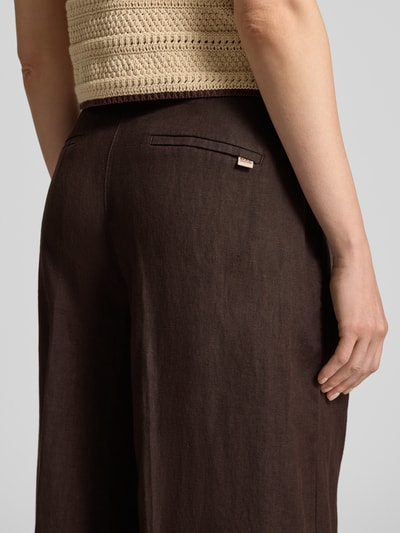 Frauenmodel trägt Leinenhose mit Label-Detail Modell 'Britt' von MAC, reine Leinen, Wide-Leg-Pants, braune Struktur, Detailaufnahme Rückansicht. Bundweite bei Größe 36/32: 40 cm, Innenbeinlänge: 82 cm, Knopfverschluss.