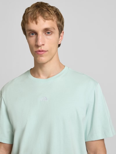 Männermodel trägt T-Shirt mit Logo-Stitching von The North Face in Hellgrün aus Baumwolle, gerader Schnitt, Nahaufnahme Oberkörper.