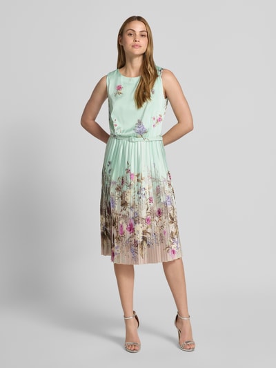 Frauenmodel trägt Knielanges Cocktailkleid mit Plisseefalten von Rinascimento, mintgrün mit Blumenmuster, A-Linie, Gürtel, Ganzkörperansicht von vorne.