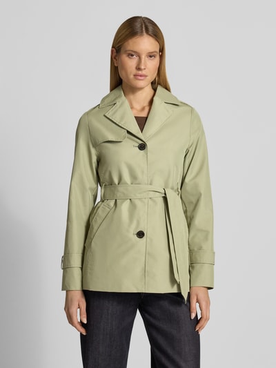 Frauenmodel trägt Regular Fit Trenchcoat aus Baumwoll-Mix von s.Oliver RED LABEL in hellem Grün, Taillengürtel, Reverskragen, Ganzkörperansicht von vorne.
