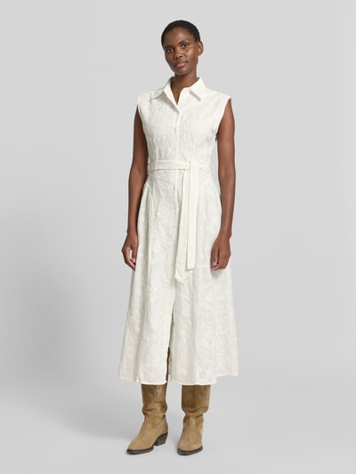 Frauenmodel trägt Maxikleid mit Bindegürtel Modell 'CATA' von Mango in Elfenbein, reine Baumwolle, tailliert, Umlegekragen, Ganzkörperansicht von vorne.
