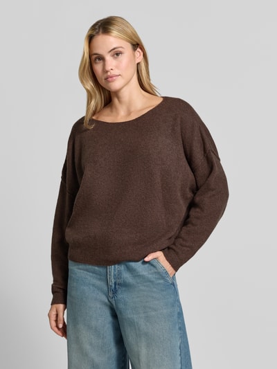 Frauenmodel trägt Relaxed Fit Strickpullover aus Material-Mix mit Leinen-Anteil von American Vintage, braun, gerippte Abschlüsse, lockere Passform, überschnittene Schultern, Rundhalsausschnitt, langärmlig, Kombi mit hellblauer Jeans, Ganzkörperansicht von vorne.