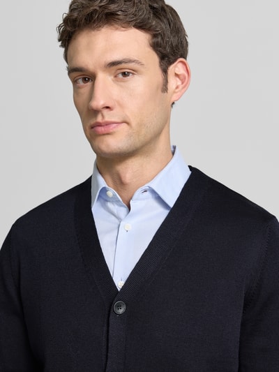 Männermodel trägt Cardigan aus Schurwolle mit V-Ausschnitt von Maerz in dunklem Blau, feine Strickstruktur, Regular-Fit, Nahaufnahme Oberkörper. Rückenlänge 68 cm, Ärmellänge 64 cm, Knopfleiste, Größe 50.