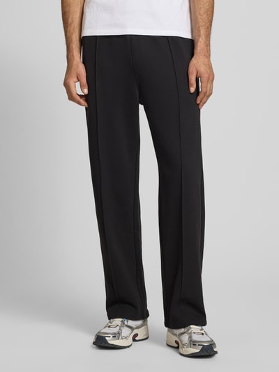 Männermodel trägt Sweatpants mit Längsnähten und Label-Stitching von CHAMPION aus Baumwoll-Mix, Relaxed-Fit, Ganzkörperansicht von vorne.