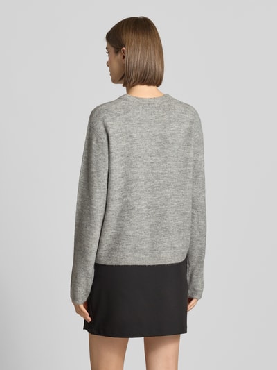 Frauenmodel trägt Loose Fit Strickjacke mit Rundhalsausschnitt Modell 'SIMONI' von ONLY in Hellgrau, kombiniert mit schwarzem Rock, Ganzkörperansicht Rückansicht, Damen Strickjacke von ONLY.
