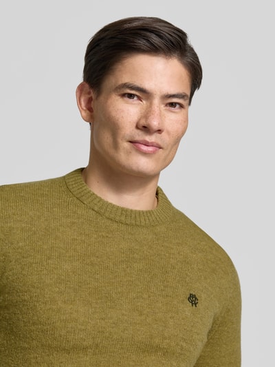 Männermodel trägt Slim Fit Strickpullover aus reiner Wolle mit Label-Stitching von MCNEAL in Olivgrün, Nahaufnahme Oberkörper, gerippte Abschlüsse, feine Wollstruktur.