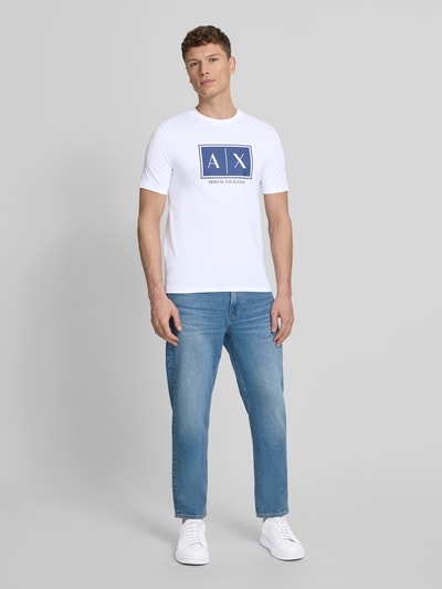 Männermodel trägt T-Shirt mit Logo und Rundhalsausschnitt von ARMANI EXCHANGE aus reiner Baumwolle, Regular-Fit, weiße und blaue Farben, Rückenlänge bei Größe M 71 cm, Ganzkörperansicht von vorne.