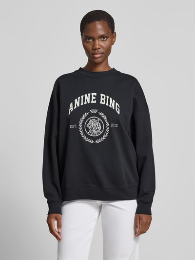 Frauenmodel trägt Oversized Fit Sweatshirt mit Logo-Print von Anine Bing in Schwarz, Reine Baumwolle, Rundhalsausschnitt, elastische Abschlüsse, Rückenlänge bei Größe S 61 cm, Ganzkörperansicht von vorne.