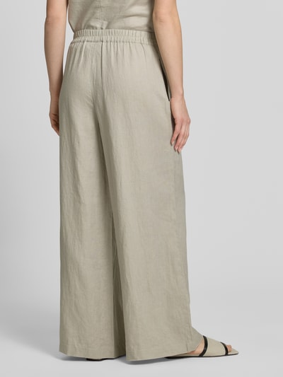 Frauenmodel trägt Leinenhose mit elastischem Bund von Style Icon Collection, beigefarbener Stoff, weiter Schnitt, reine Leinenstruktur, Ganzkörperansicht Rückansicht.
